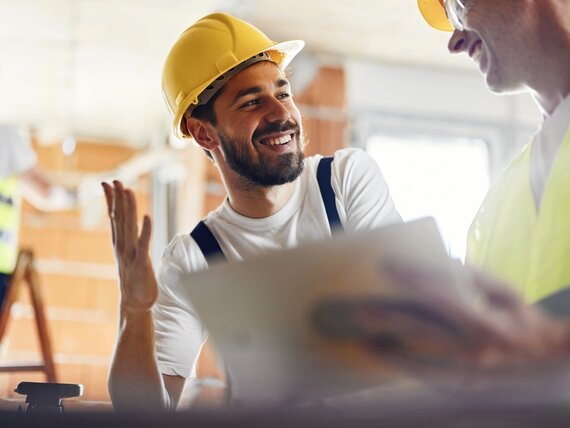 Zwei Männer mit Schutzhelmen unterhalten sich auf einer Baustelle