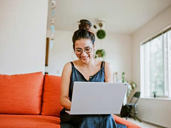 Eine Frau sitzt mit ihrem Laptop auf einem Sofa.