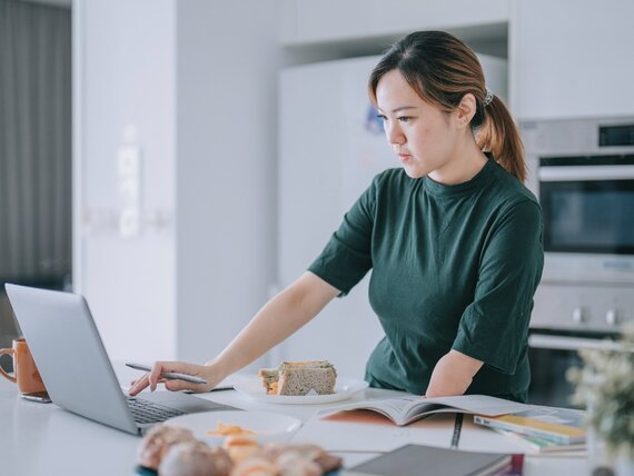 Eine Frau mit einem amputiertem Arm steht in der Küche und arbeitet am Laptop.