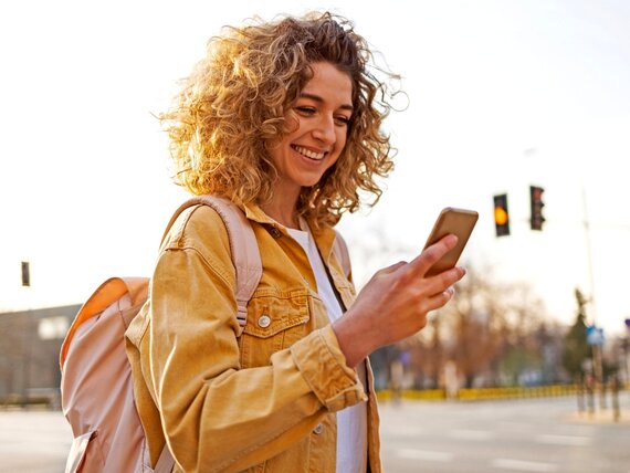 Eine Frau mit Rucksack ist draußen unterwegs und schaut auf ihr Smartphone.