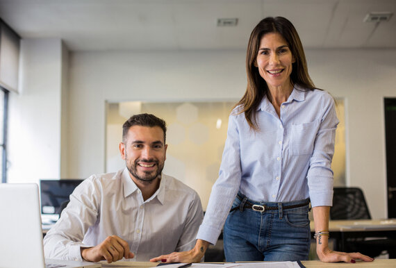 Ein sitzender Mann und eine stehende Frau in einem Büro.
