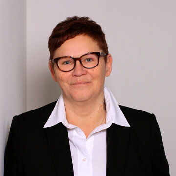 Portrait der Teamassistentin Claudi Michel. Eine Frau mit kurzen, braunen Haaren und Brille, die freundlich in die Kamera schaut.