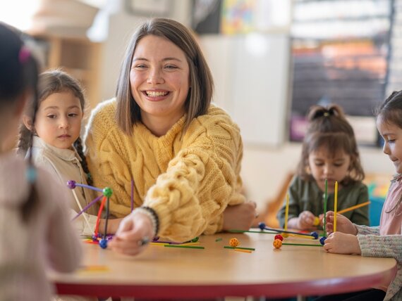 Eine junge, fröhliche Erzieherin spielt mit einer Gruppe Kleinkinder in der Kita