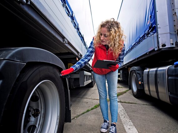 Eine Frau steht zwischen zwei LKW und kontrolliert die Reifen.