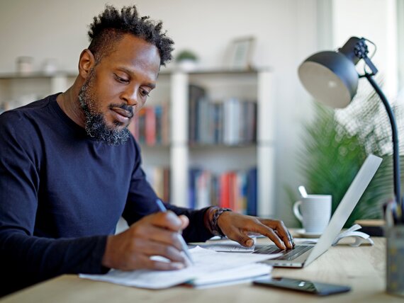 Ein Mann sitzt am Schreibtisch und macht sich Notizen.