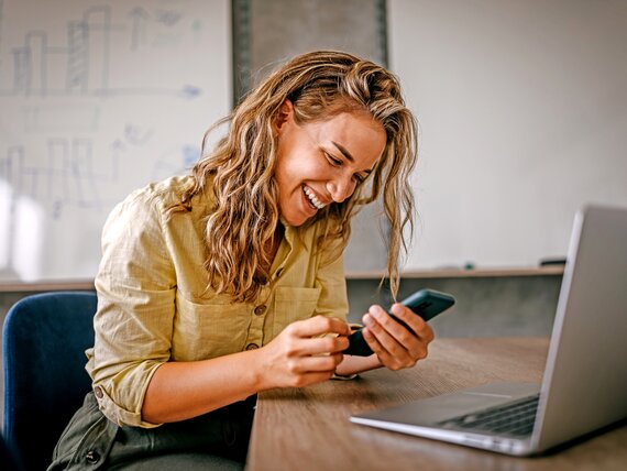 Eine Frau schaut auf ihr Smartphone und lacht fröhlich.