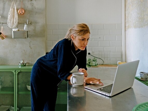 Eine Frau im Pyjama steht in der Küche vor ihrem Laptop.