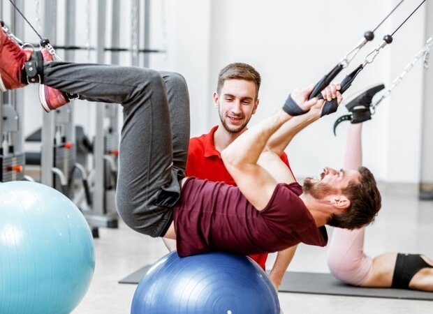 Ein junger Physiotherapeut macht mit seinem Patienten Übungen auf Gymnastikbällen