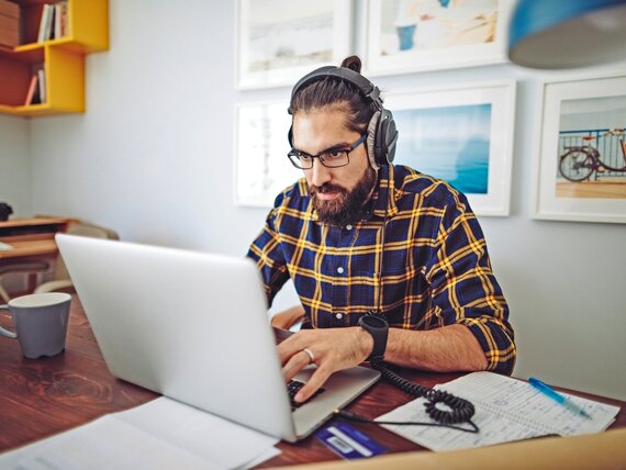 Ein Mann mit Kopfhörern arbeitet konzentriert an seinem Laptop.