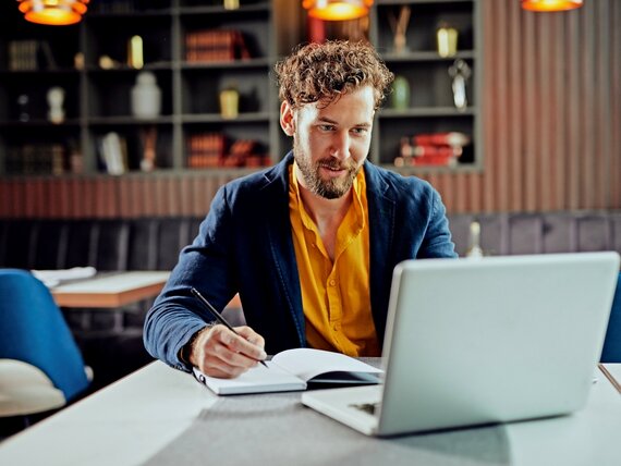Ein Mann sitzt in einem Café und arbeitet an seinem Laptop.
