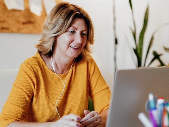 Eine Frau mit Kopfhörern sitzt vor ihrem Laptop und nimmt an einem Videocall teil.