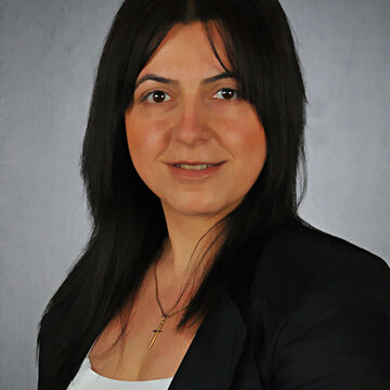 Eine Frau mit schwarzen Haaren, schwarzem Blazer und weißem Oberteil.