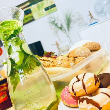 Eine Karaffe mit Wasser, Minze und Limetten. Daneben ein Teller mit Donuts und eine Schüssel mit Baguettes.