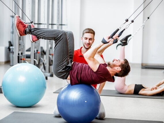 Ein junger Physiotherapeut macht mit seinem Patienten Übungen auf Gymnastikbällen