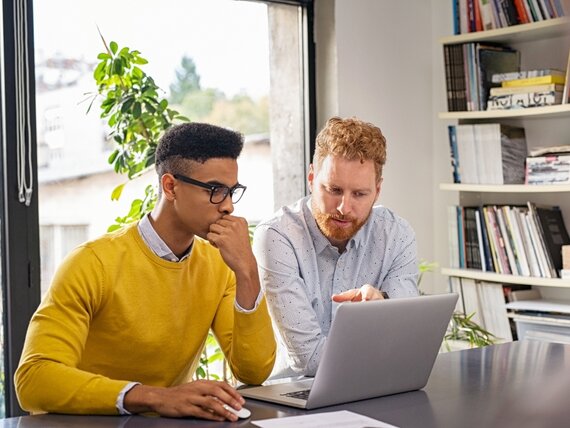 Zwei Männer arbeiten gemeinsam an einem Laptop.