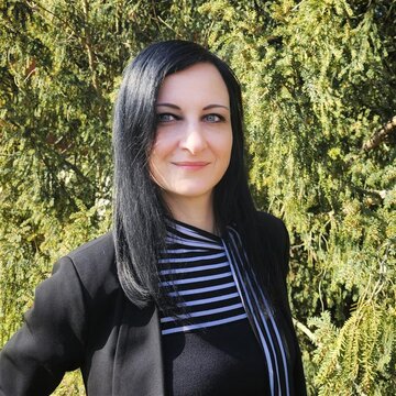 Frau mit schwarzen Haar lächelt freundlich und steht vor einem grünen Hintergrund