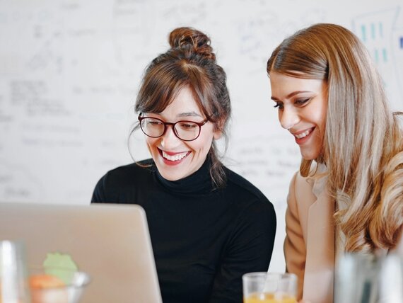 Zwei fröhliche Frauen schauen sich etwas auf einem Laptop an.