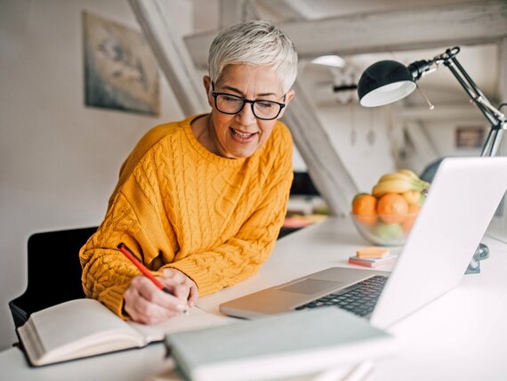 Eine Frau im Homeoffice arbeitet am Laptop und macht sich Notizen.