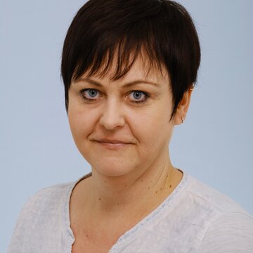 Frau mit kurzem Haar und großen blauen Augen schaut freundlich.