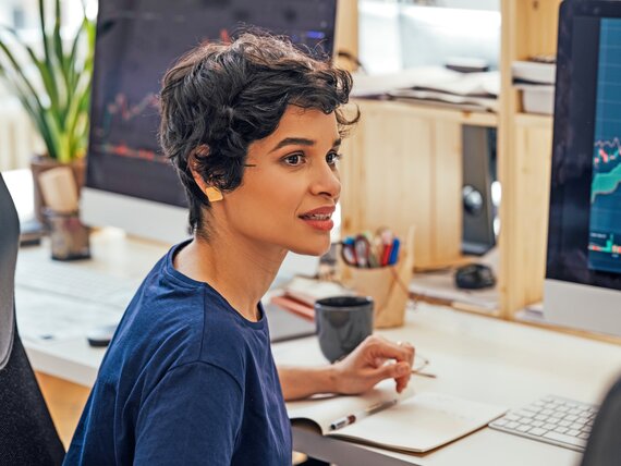 Eine Frau sitzt vor 2 Computerbildschirmen und schaut sich Graphen an.