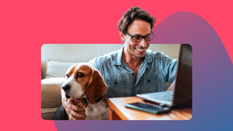 Mann mit Brille sitzt lächelnd auf dem Fußboden, an ein Sofa angelehnt, vor ihm ein Laptop auf einem Couchtisch, ein Hund sitzt neben ihm.