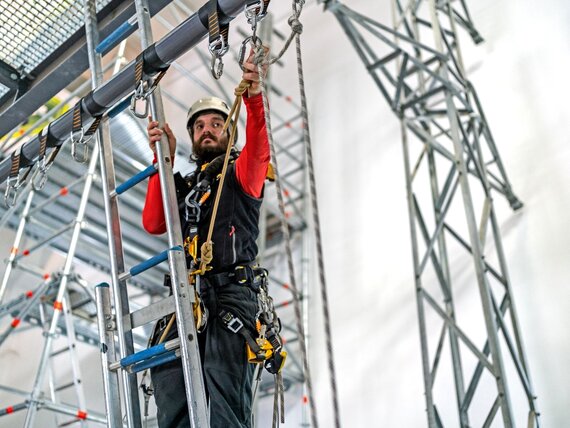 Ein Mann mit Sturzhelm und Schutzkleidung arbeitet an einem Gerüst