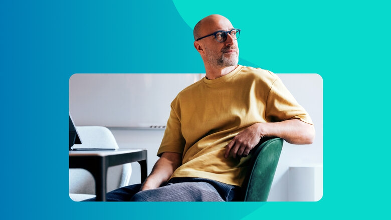 Mann mit Brille in gelbem T-Shirt sitzt auf einem Stuhl und schaut nachdenklich