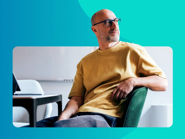 Mann mit Brille in gelbem T-Shirt sitzt auf einem Stuhl und schaut nachdenklich