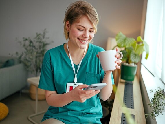 Eine junge Plfegerin macht eine Pause und trinkt einen Kaffee während sie ihr Smartphone benutzt