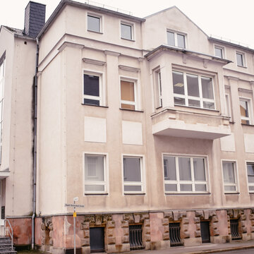 gelbes Gebäude mit mehreren Fenstern und einem gläsernen Eingang auf der linken Seite mit Treppe.