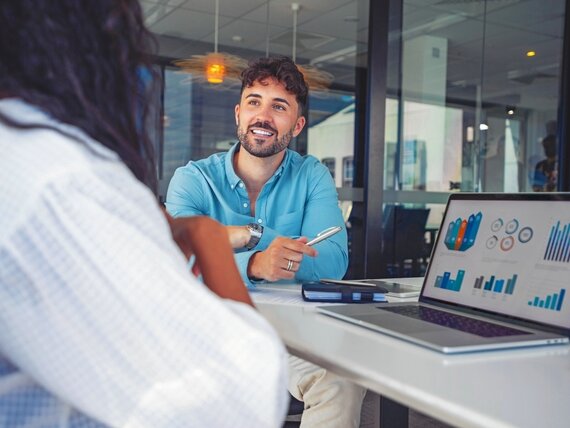 Eine Frau und ein Mann besprechen Diagramme am Laptop.