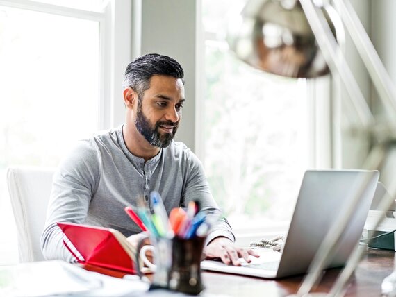 Ein Mann arbeitet im Homeoffice an seinem Laptop und macht sich Notizen.