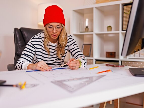 Eine junge Architektin sitzt am Schreibtisch und arbeitet an ihren Zeichnungen.