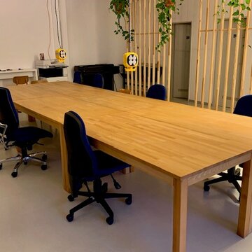 Ein langer Holztisch mit Bürostühlen. Darüber hängen Steckdosenboxen von der Wand.