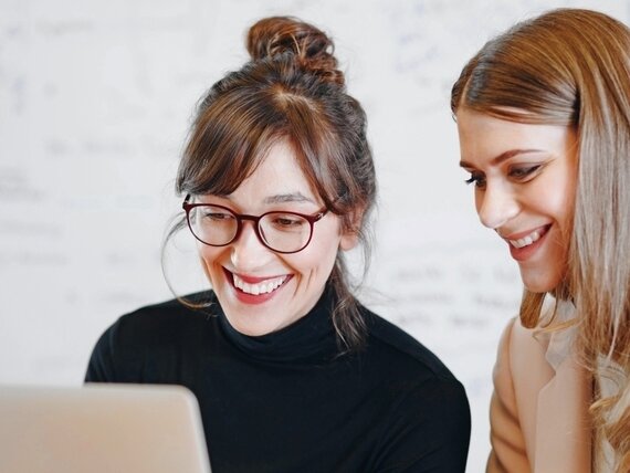 Zwei fröhliche Frauen schauen sich etwas auf einem Laptop an.