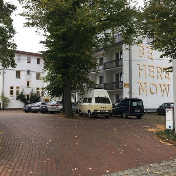 Außenansicht vom Gebäude mit einigen Bäumen und Autos davor.