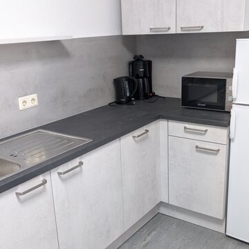 Weiße Küche mit Kaffeemaschine, Wasserkocher, Mikrowelle und Kühlschrank.