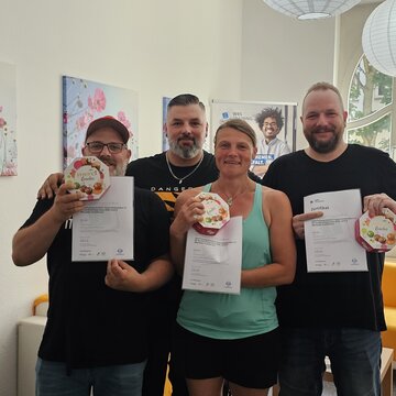 Gruppenbild von 4 Teilnehmer:innen, die ihr Zertifikat sowie eine Pralinenschachtel in den Händen halten.