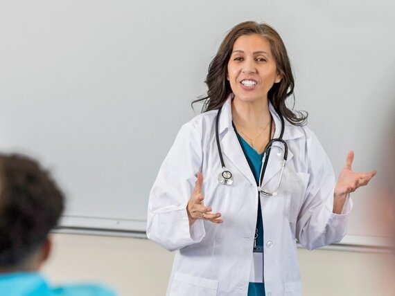 Eine Ärztin steht in einem Schulungsraum und hält einen Vortrag für Schüler und Schülerinnen