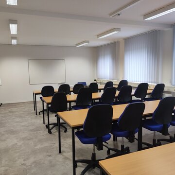 Schulungsraum für den Präsenzunterricht mit 4 Tischreihen und den dazugehörigen Bürostühlen.