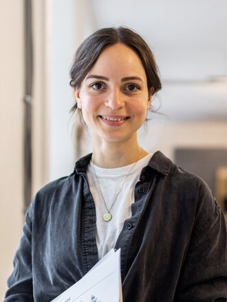 Ein Portrait einer lächelnden Frau mit einem Ordner in der Hand.