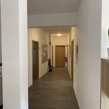 Ein langer Flur mit weißen Wänden. Links und rechts gehen Holztüren zu den Räumen ab. Es sind 2 Feuerlöcher vorhanden.