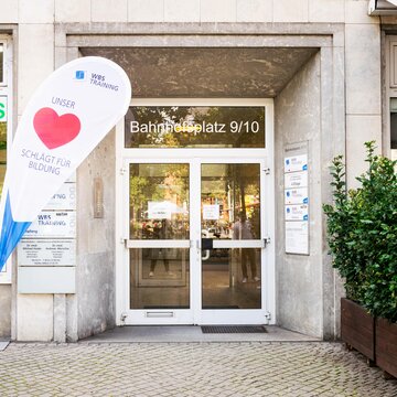 Eingangstür von außen mit Fahnenständer auf dem ein großes rotes Herz und die Aufschrift unser Herz schlägt für Bildung zu sehen ist.