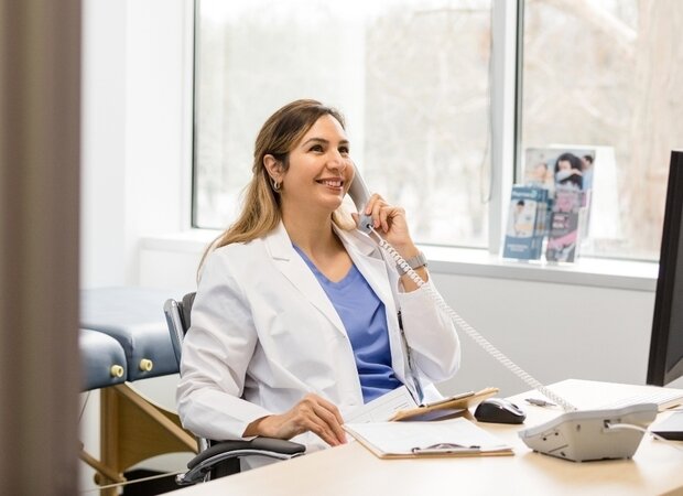 Eine fröhliche Ärztin sitzt in ihrem Büro und telefoniert