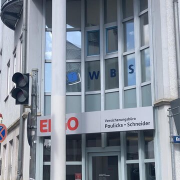 verglaster Haupteingang mit Säule im Vordergrund. Links im Bild ist eine Ampel zu sehen.