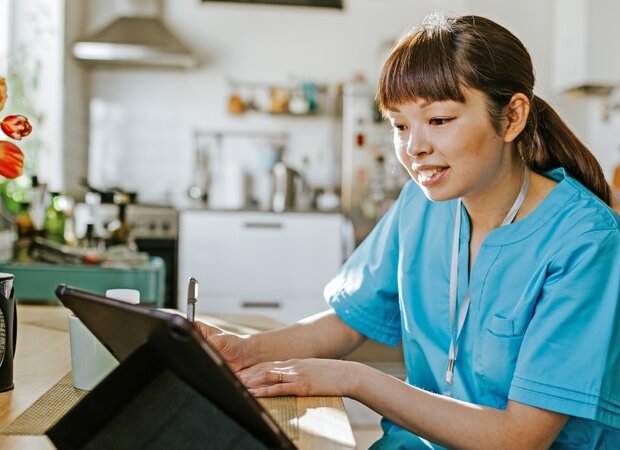 Eine Frau sitzt mit einem Tablet in der Küche und macht sich Notizen.
