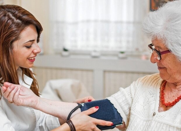 Eine junge Pflegerin misst den Blutdruck bei einer Seniorin