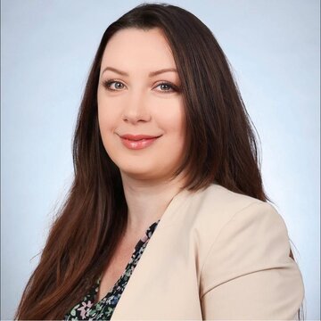 Eine Frau mit langen braunen Haaren und weißem Blazer.