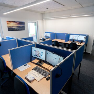 Arbeitsplätze mit 2 PC-Bildschirmen Tastatur und Maus, blauen Bürostühlen und blauen Trennwänden.