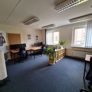 Arbeitsraum mit mehreren PC-Arbeitsplätzen, Regalen und Grünpflanzen.